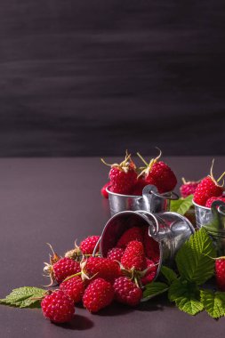 Siyah taştan bir arka planda olgun ahududular. Küçük kovalar, taze yapraklar, yeni hasat. Modaya uygun sert ışık, karanlık gölgeler, metin için yer