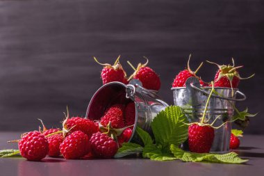 Siyah taştan bir arka planda olgun ahududular. Küçük kovalar, taze yapraklar, yeni hasat. Modaya uygun sert ışık, karanlık gölgeler, metin için yer