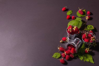 Siyah taştan bir arka planda olgun ahududular. Küçük kovalar, taze yapraklar, yeni hasat. Modaya uygun sert ışık, karanlık gölgeler, metin için yer