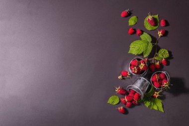 Siyah taştan bir arka planda olgun ahududular. Küçük kovalar, taze yapraklar, yeni hasat. Modaya uygun sert ışık, karanlık gölgeler, üst manzara