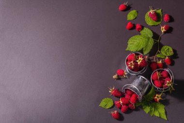 Siyah taştan bir arka planda olgun ahududular. Küçük kovalar, taze yapraklar, yeni hasat. Modaya uygun sert ışık, karanlık gölgeler, üst manzara