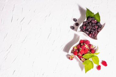 Çeşit çeşit kırmızı ve siyah ahududu. Seramik kaseler, modern sert ışık, karanlık gölge. Beyaz mutfak arka planı, üst görünüm