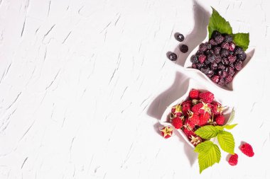 Çeşit çeşit kırmızı ve siyah ahududu. Seramik kaseler, modern sert ışık, karanlık gölge. Beyaz mutfak arka planı, üst görünüm