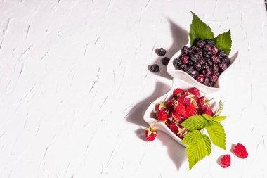 Çeşit çeşit kırmızı ve siyah ahududu. Seramik kaseler, modern sert ışık, karanlık gölge. Beyaz mutfak arka planı, kapat