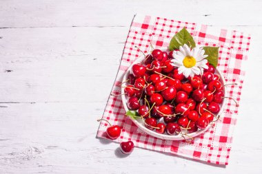 Bir kase dolusu su damlacıklarıyla taze kirazlar. Eski beyaz ahşap masa, üst manzara.