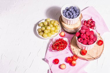 Çeşit çeşit olgun böğürtlen kaseleri. Taze ahududu, yabanmersini, üzüm, tatlı kiraz ve kırmızı frenk üzümü. Beyaz alçı arkaplan, metin için yer