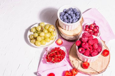 Çeşit çeşit olgun böğürtlen kaseleri. Taze ahududu, yabanmersini, üzüm, tatlı kiraz ve kırmızı frenk üzümü. Beyaz alçı arkaplan, metin için yer