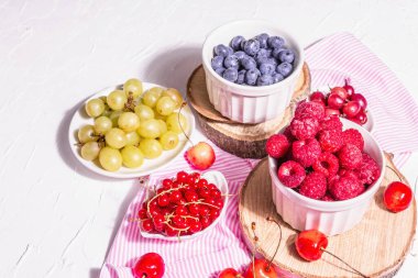 Çeşit çeşit olgun böğürtlen kaseleri. Taze ahududu, yabanmersini, üzüm, tatlı kiraz ve kırmızı frenk üzümü. Beyaz alçı arkaplan, metin için yer