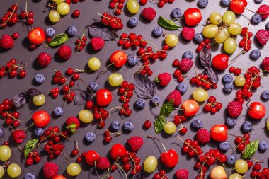 Değişik olgun meyveler, siyah bir taşın üzerine serpiştirilmiş. Taze ahududu, yabanmersini, üzüm, tatlı kiraz ve kırmızı frenk üzümü. Modern sert bir ışık, karanlık bir gölge, üst manzara.