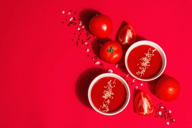 Kırmızı arka planda susam tohumlu domates çorbası. Olgun sebzeler, gül Himalaya tuzu, pembe karabiber. Modern sert bir ışık, karanlık bir gölge, üst manzara.