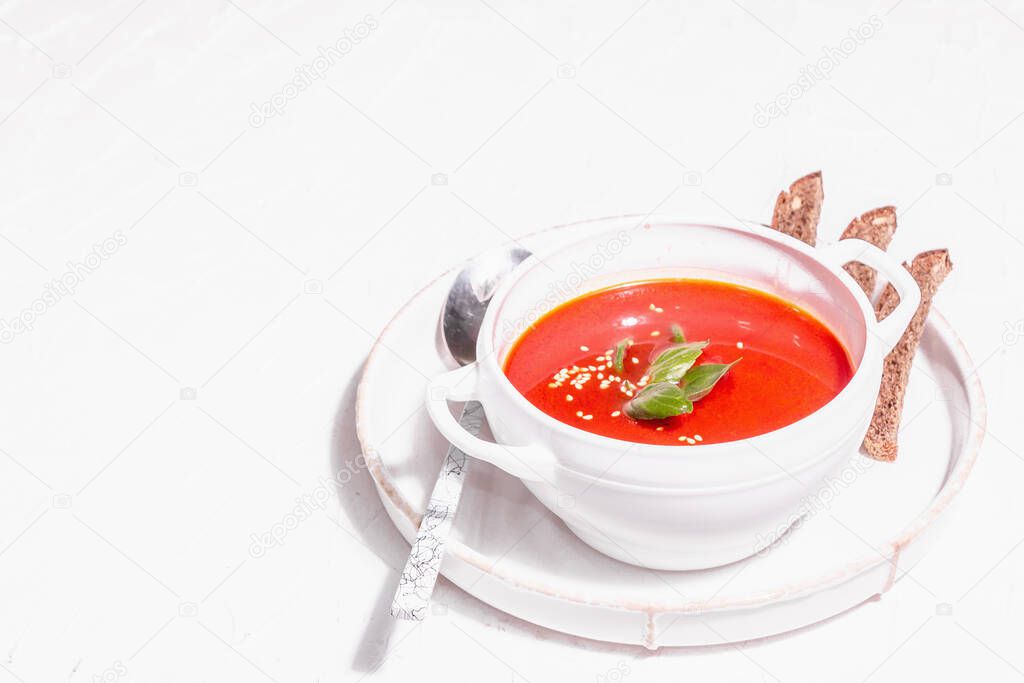 Red puree soup with tomato, greens, and bread. Trendy hard light, dark shadow. White putty background, copy space
