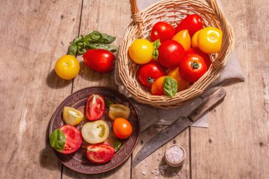 Taze fesleğenli olgun domatesler. Hasat sepetindeki yeni sebzeler. Eski ahşap zemin, üst manzara