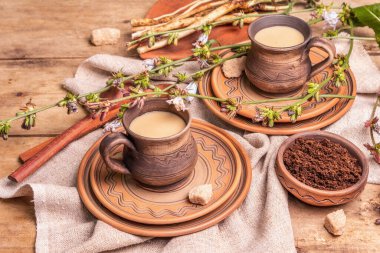 Tahta bir masada seramik bardaklarda sıcak doğal hindiba kafeini. Kahve ve kafein için sağlıklı bir alternatif. Mavi hindiba çiçekleri, taze kökler, yakın plan.