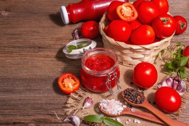 Domates şenliği, reçel, turşu, cam kavanozdaki sos. Ev yapımı koruma konsepti. Taze domates, baharat, sarımsak, yeşillik, deniz tuzu. Modern sert ışık, karanlık gölge, eski ahşap masa, kopyalama alanı