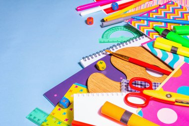 Mavi arka planda kırtasiye aksesuarı. Okul malzemeleri, kalemler, boyalar, makas ve renkli defterler. Eğitim ve serbest çalışma kavramı, kopyalama alanı