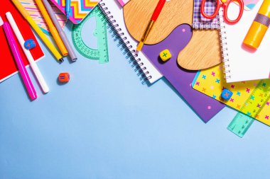 Mavi arka planda kırtasiye aksesuarı. Okul malzemeleri, kalemler, boyalar, makas ve renkli defterler. Eğitim ve serbest çalışma konsepti, üst görünüm