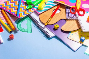 Mavi arka planda kırtasiye aksesuarı. Okul malzemeleri, kalemler, boyalar, makas ve renkli defterler. Eğitim ve serbest çalışma kavramı, kopyalama alanı