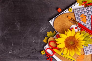 Siyah karatahta üzerine okul malzemeleri. Albüm, defter, palet, makas, fırça ve ayçiçeği içeren kompozisyon. Okul konseptine geri dön, üst görünüm