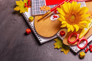 Siyah karatahta üzerine okul malzemeleri. Albüm, defter, palet, makas, fırça ve ayçiçeği içeren kompozisyon. Okul konseptine geri dön, alanı kopyala