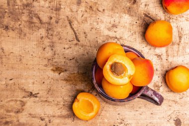 Eski bir demir kupada olgun kayısılar. Tatlı meyveler, eski ahşap masa, üst manzara.