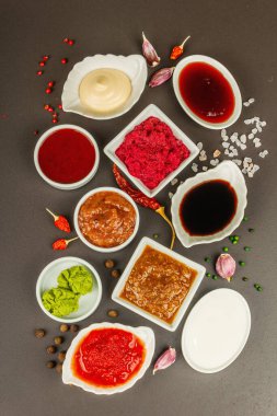 Farklı soslar - ketçap, mayonez, barbekü, soya, turşu, wasabi, adjika, yaban turpu, aioli, marinara. Koyu taş zemin, üst görünüm