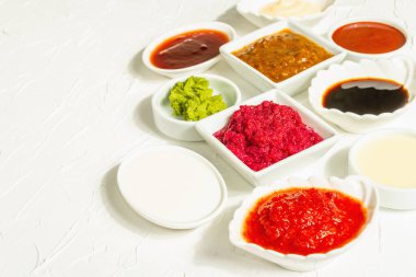 Farklı soslar - ketçap, mayonez, barbekü, soya, turşu, wasabi, adjika, yaban turpu, aioli, marinara. Modaya uygun sert ışık, karanlık gölge. Beyaz macun arkaplanı, kapat