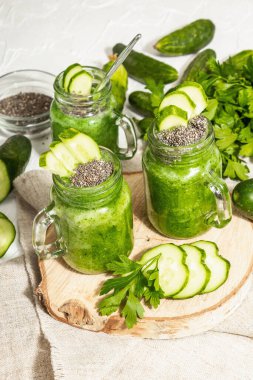 Cam kavanozda salatalıklı yeşil smoothie. Taze sebzeler, yeşiller ve chia tohumları. Modaya uygun sert ışık, karanlık gölge. Beyaz macun arkaplanı, kapat