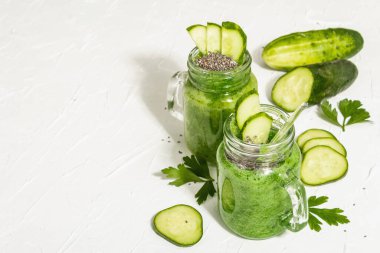 Cam kavanozda salatalıklı yeşil smoothie. Taze sebzeler, yeşiller ve chia tohumları. Modaya uygun sert ışık, karanlık gölge. Beyaz macun arkaplanı, kopyalama alanı