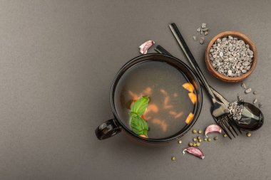 Sebzeli şeffaf tavuk çorbası. Geleneksel bulyon, sağlıklı yemek, çatal bıçak takımı. Siyah taş arkaplan, üst görünüm