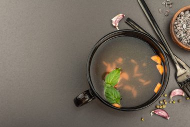 Sebzeli şeffaf tavuk çorbası. Geleneksel bulyon, sağlıklı yemek, çatal bıçak takımı. Siyah taş arkaplan, üst görünüm