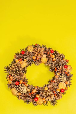 Sonbahar koni, fıstık ve böğürtlen çelengi. Yaratıcı kompozisyon, el yapımı. Ev dekorasyonu festivali konsepti. Parlak sarı arkaplan, üst görünüm