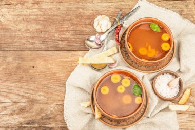 Seramik kaselerde sebzeli şeffaf tavuk suyu çorbası. Geleneksel bulyon, sağlıklı yemek, çatal bıçak takımı. Eski ahşap zemin, üst manzara