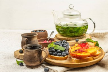 Krem peynirli ve olgun meyveli tost ekmeği. Izgara şeftali, yabanmersini ve arkaplanda nane çayı. Yararlı kahvaltı kavramı, kopyalama alanı