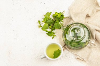 Hafif arka planda mis kokulu nane çayı. Cam çaydanlık, bir fincan çay, bir demet taze nane. Günaydın konsept, üst görünüm