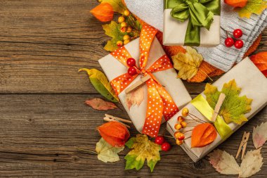 Sonbahar tasarımlı sıfır atık hediye konsepti. Sıcak kazaklar, dökülen yapraklar, tematik dekorasyon. Yumuşak ışık, eski tahta arka plan, üst manzara