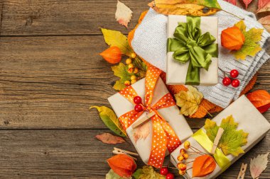 Sonbahar tasarımlı sıfır atık hediye konsepti. Sıcak kazaklar, dökülen yapraklar, tematik dekorasyon. Yumuşak ışık, eski tahta arka plan, üst manzara