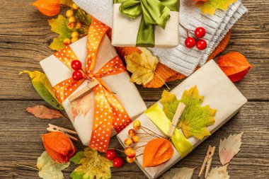 Sonbahar tasarımlı sıfır atık hediye konsepti. Sıcak kazaklar, dökülen yapraklar, tematik dekorasyon. Yumuşak ışık, eski tahta arka plan, üst manzara