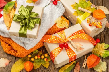 Sonbahar tasarımlı sıfır atık hediye konsepti. Sıcak kazaklar, dökülen yapraklar, tematik dekorasyon. Yumuşak ışık, eski tahta arka plan, üst manzara