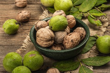 Olgun kahverengi ve olgunlaşmamış yeşil cevizler bir kasede. Eski ahşap arka plan, kapat