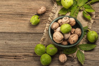 Olgun kahverengi ve olgunlaşmamış yeşil cevizler bir kasede. Eski ahşap zemin, üst manzara