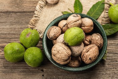 Olgun kahverengi ve olgunlaşmamış yeşil cevizler bir kasede. Eski ahşap zemin, üst manzara