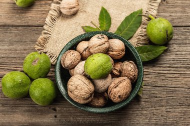 Olgun kahverengi ve olgunlaşmamış yeşil cevizler bir kasede. Eski ahşap zemin, üst manzara