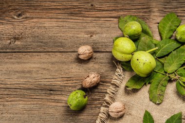 Olgun kahverengi ve olgunlaşmamış yeşil cevizler çuval bezi peçetede. Eski ahşap zemin, üst manzara