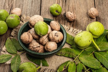 Olgun kahverengi ve olgunlaşmamış yeşil cevizler bir kasede. Eski ahşap arka plan, kapat