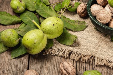 Olgun kahverengi ve olgunlaşmamış yeşil cevizler çuval bezi peçetede. Eski tahta arkaplan, kopyalama alanı