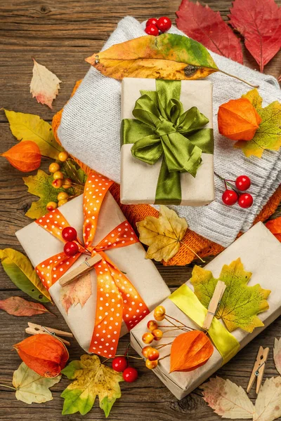 Sonbahar tasarımlı sıfır atık hediye konsepti. Sıcak kazaklar, dökülen yapraklar, tematik dekorasyon. Yumuşak ışık, eski tahta arka plan, üst manzara