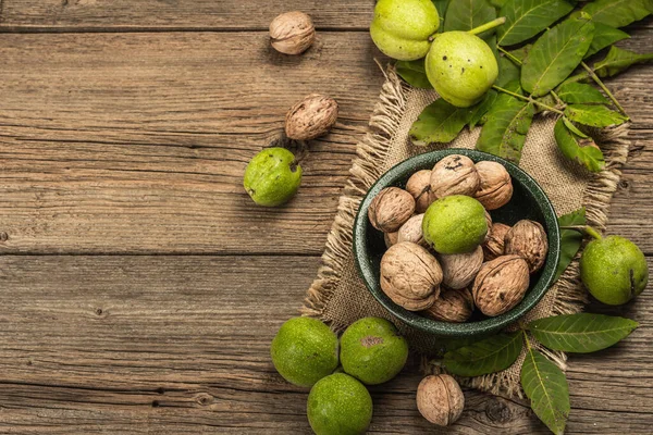 Olgun kahverengi ve olgunlaşmamış yeşil cevizler bir kasede. Eski ahşap zemin, üst manzara
