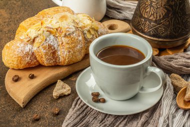 Kahve ve kruvasan, günaydın ve kahvaltı konsepti. Kahveli bakır Türk, sütlü sürahi, kahve çekirdekleri. Kahverengi taş beton arka plan, kapat