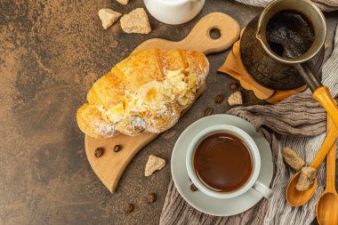 Kahve ve kruvasan, günaydın ve kahvaltı konsepti. Kahveli bakır Türk, sütlü sürahi, kahve çekirdekleri. Kahverengi taş arkaplan, üst görünüm