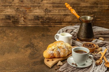 Kahve ve kruvasan, günaydın ve kahvaltı konsepti. Kahveli bakır Türk, sütlü sürahi, kahve çekirdekleri. Kahverengi taş arkaplan, kopyalama alanı